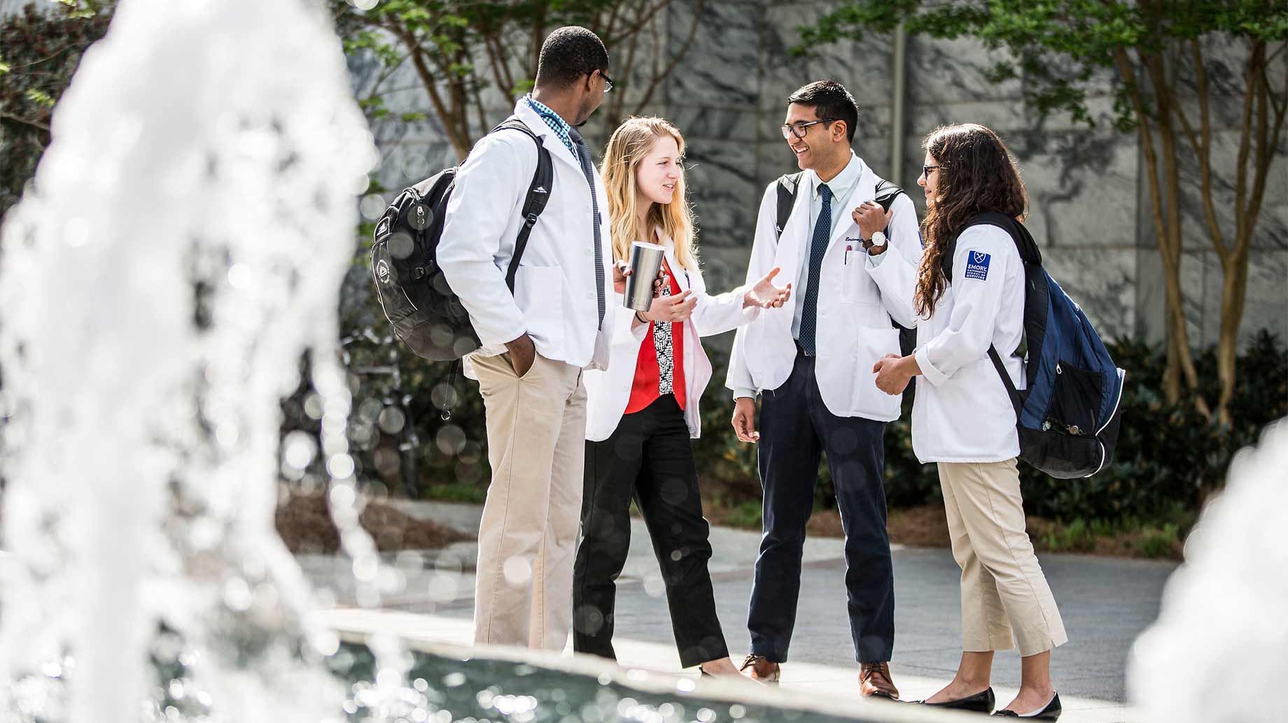 four medical students standing and conversing beside a fountain