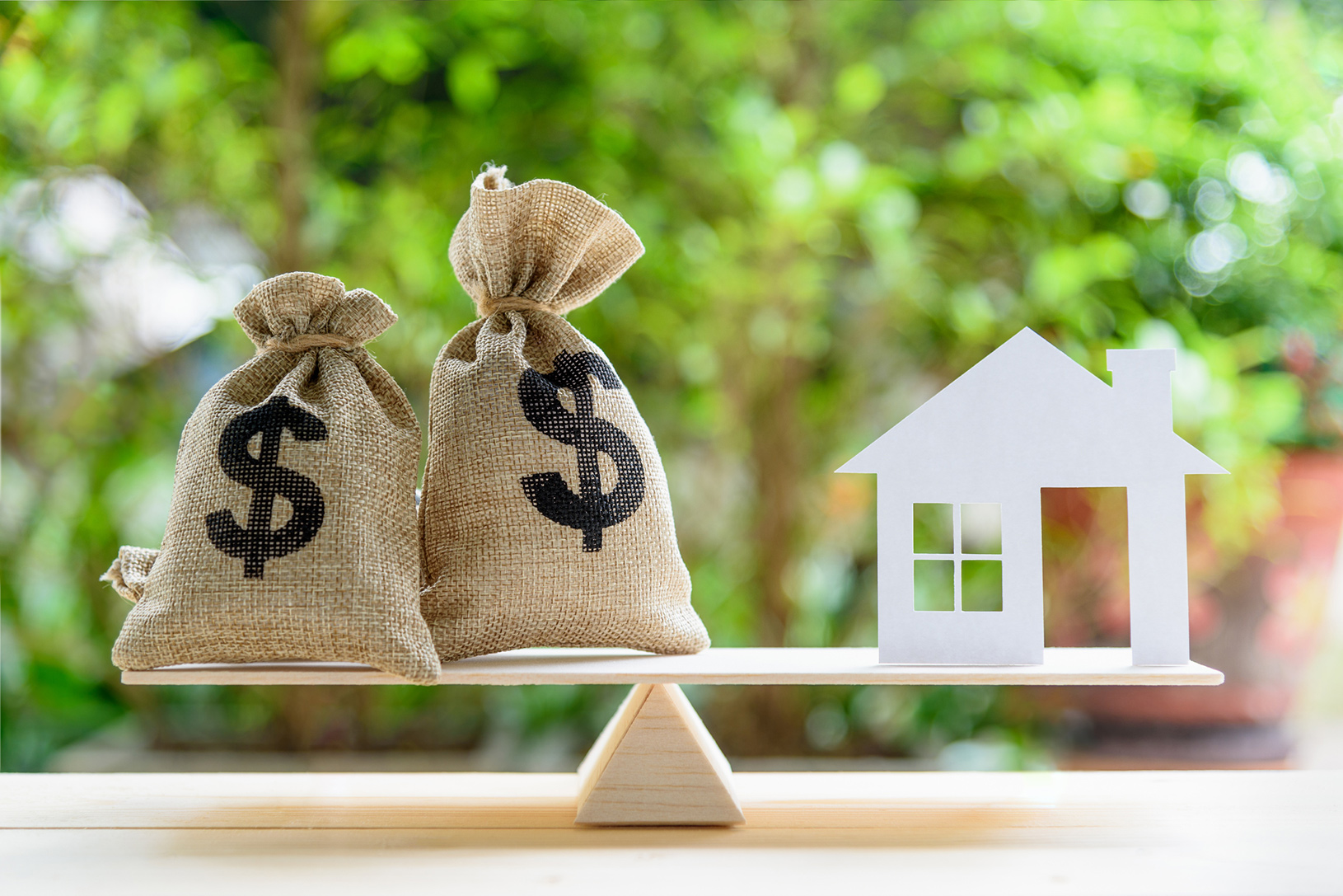 money bags balanced on scale with replica of home