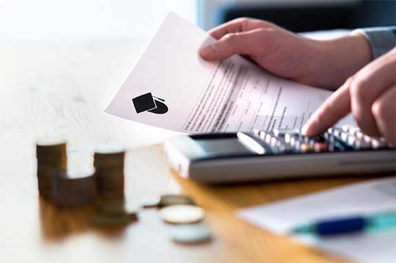 hands holding college letter with calculator and stacks of coins in foreground